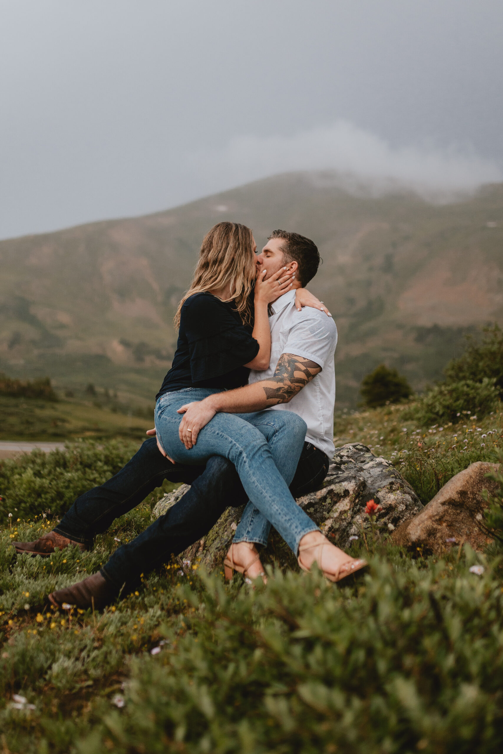 a couple sitting on a rock kissing